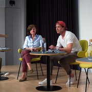 Marina Villa und Kevin Lötscher sitzen an einem Tisch auf einer Bühne. Beide haben ein Buch vor sich. 